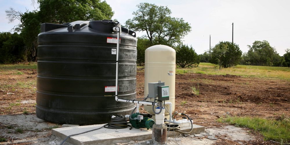 Deep water well set up, country side construction. Drilled draw well with pressure switch and storage tank.
